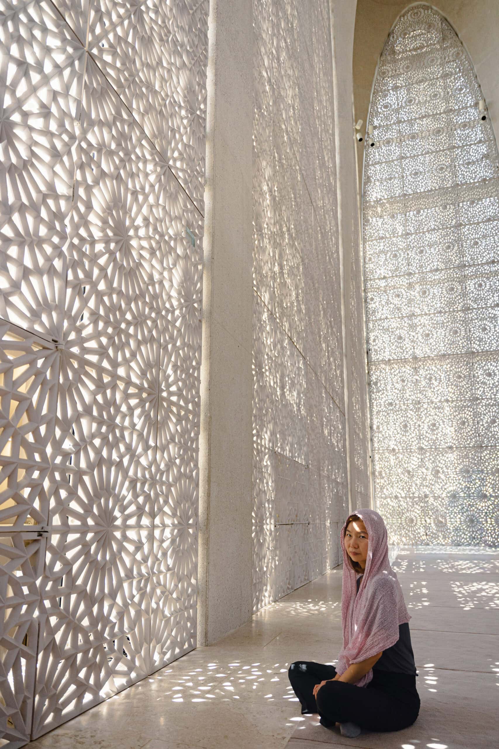 Jin sits on the carpet, head covered with a scarf inside the mosque of the Abrahamic Family House Abu Dhabi