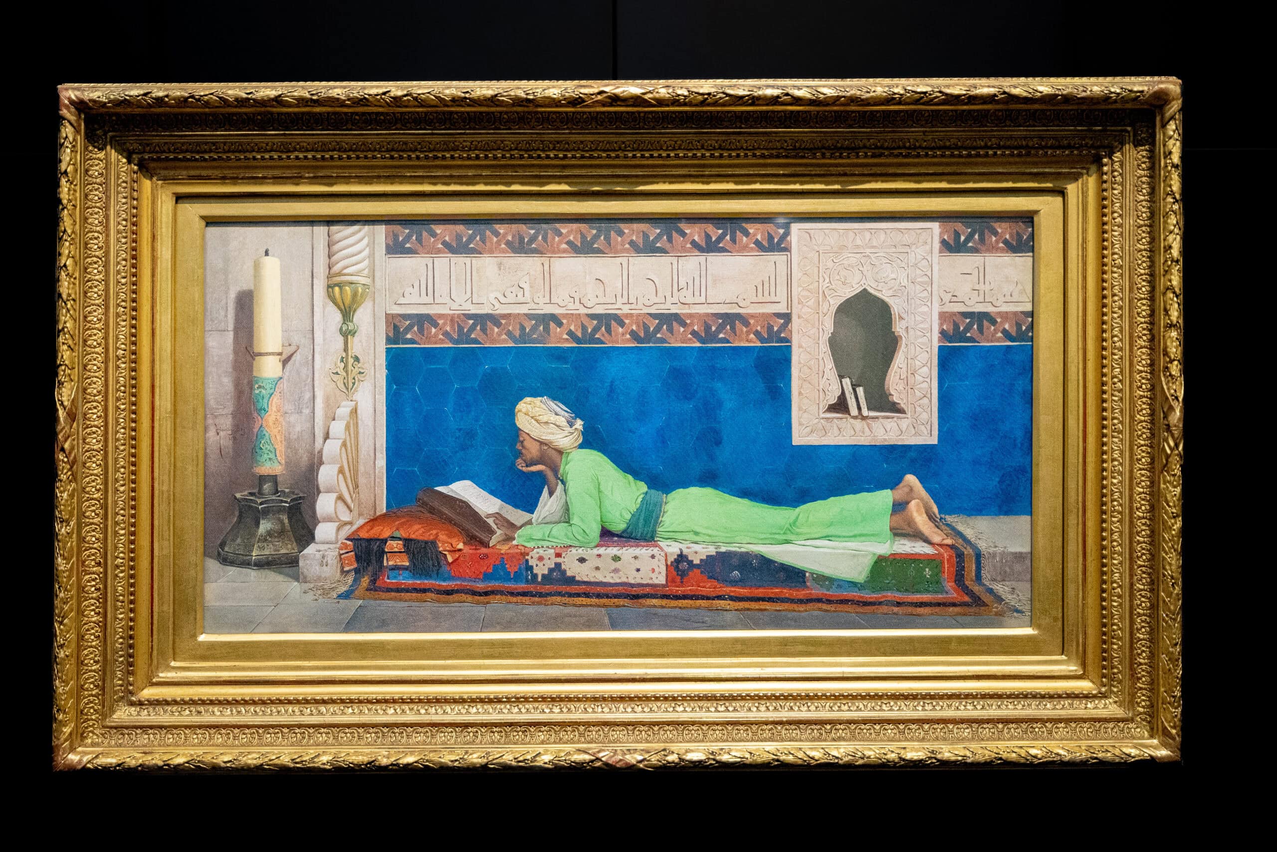 Young Emir Studying, a beautiful painting of a young man lying down on his stomach with his hand under his chin, reading
