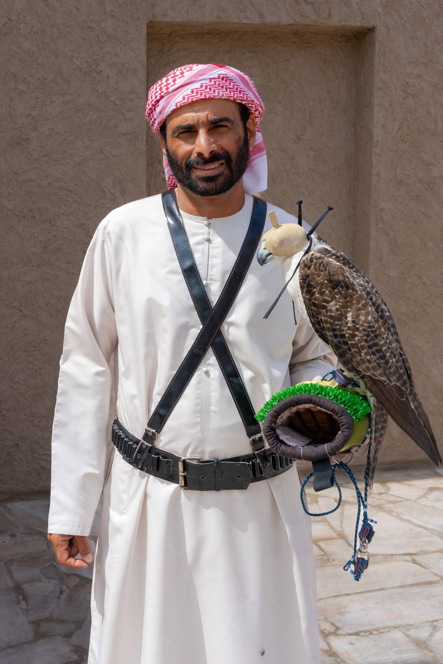 A man with a beard and and a white and red headdress in traditional Emirati dress holds a falcon in Old Dubai