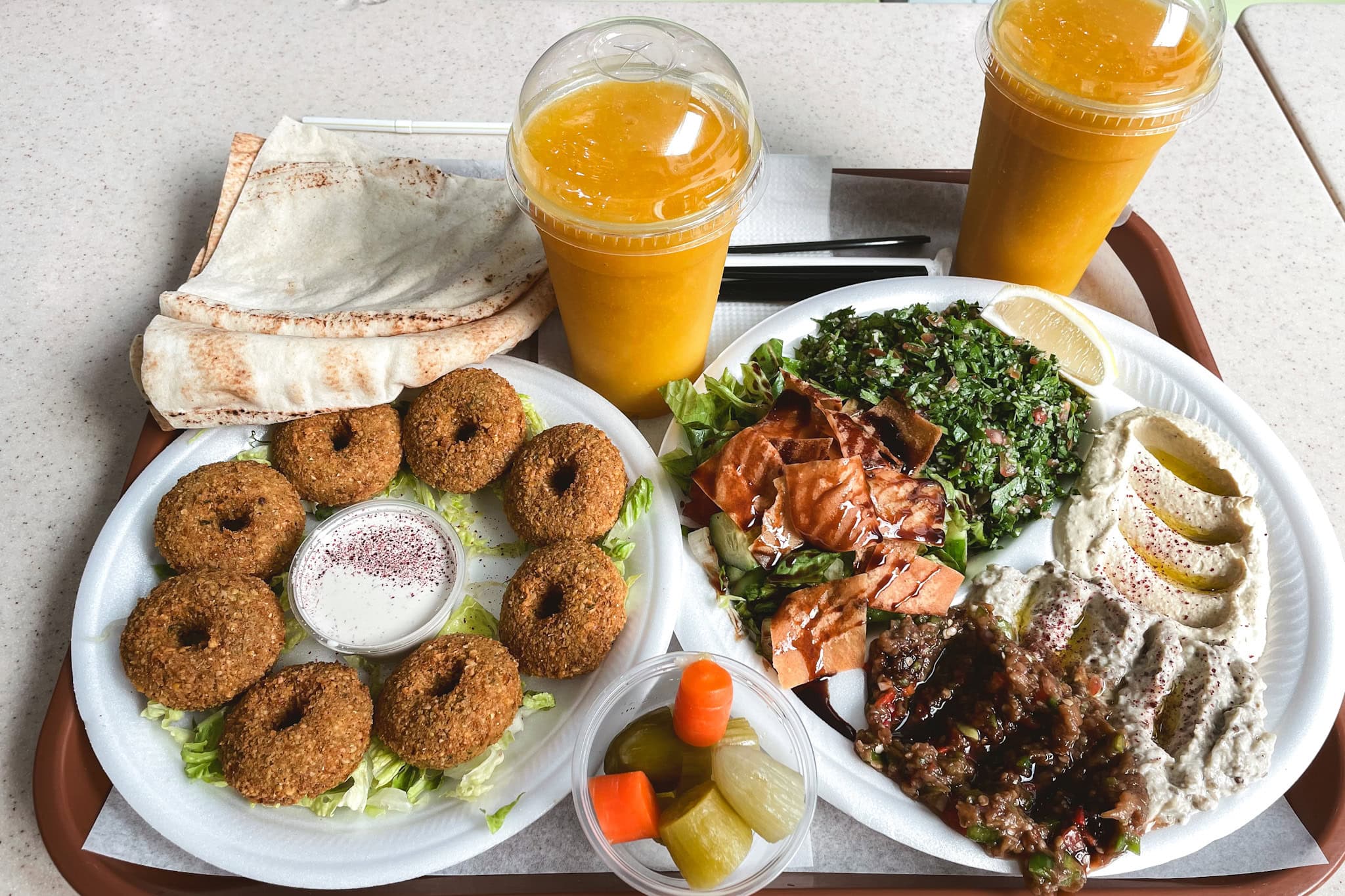 Middle eastern breakfast from a cafeteria in Abu Dhabi. There are fried falafel, flat bread, hummus, moutabal, fatoush, tabbouleh, and two glasses with freshly squeezed orange juice