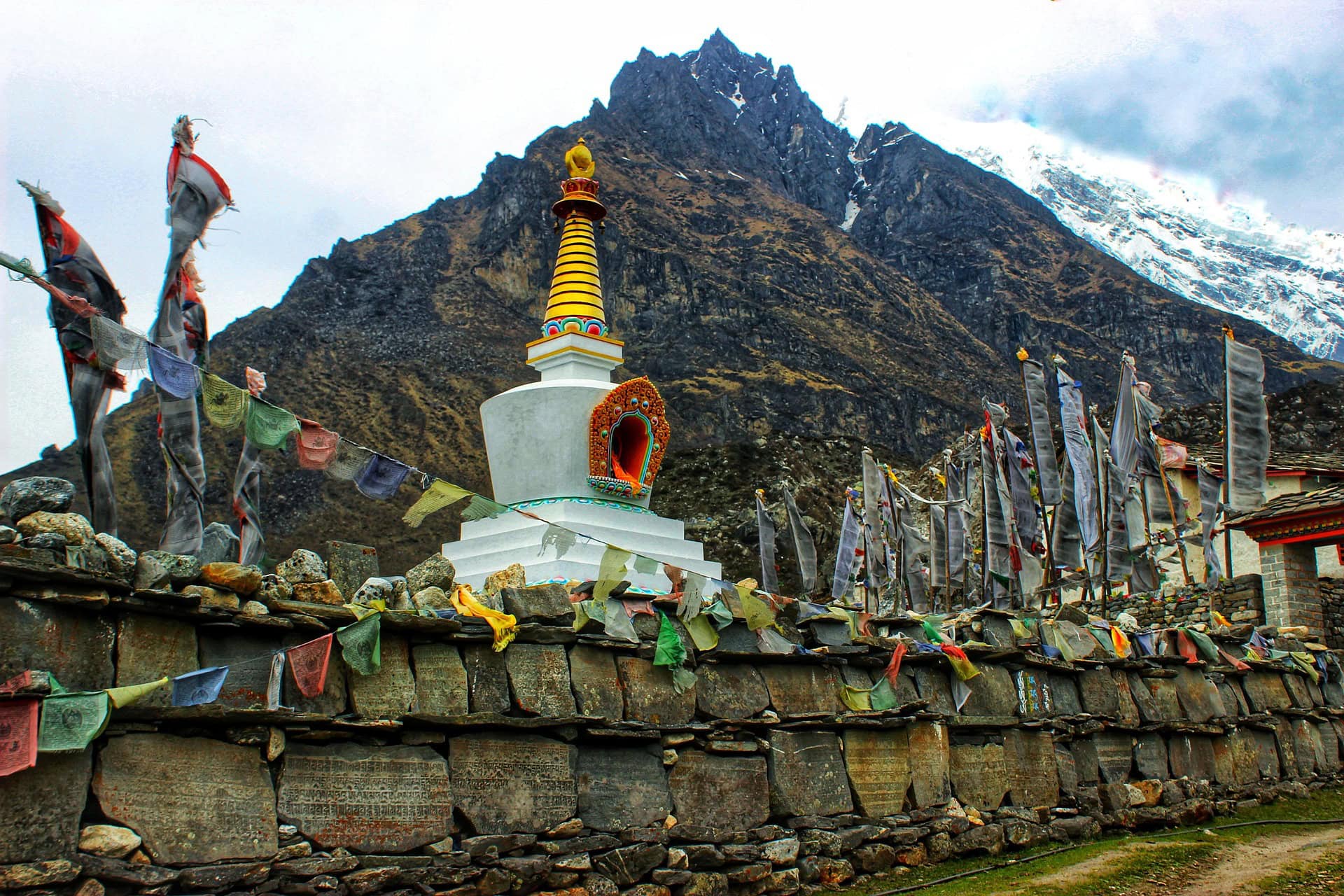 Colorful prayer flags and a stupa in a Himalayan village with snow-capped mountains in the background, seen on the Langtang Valley Trek