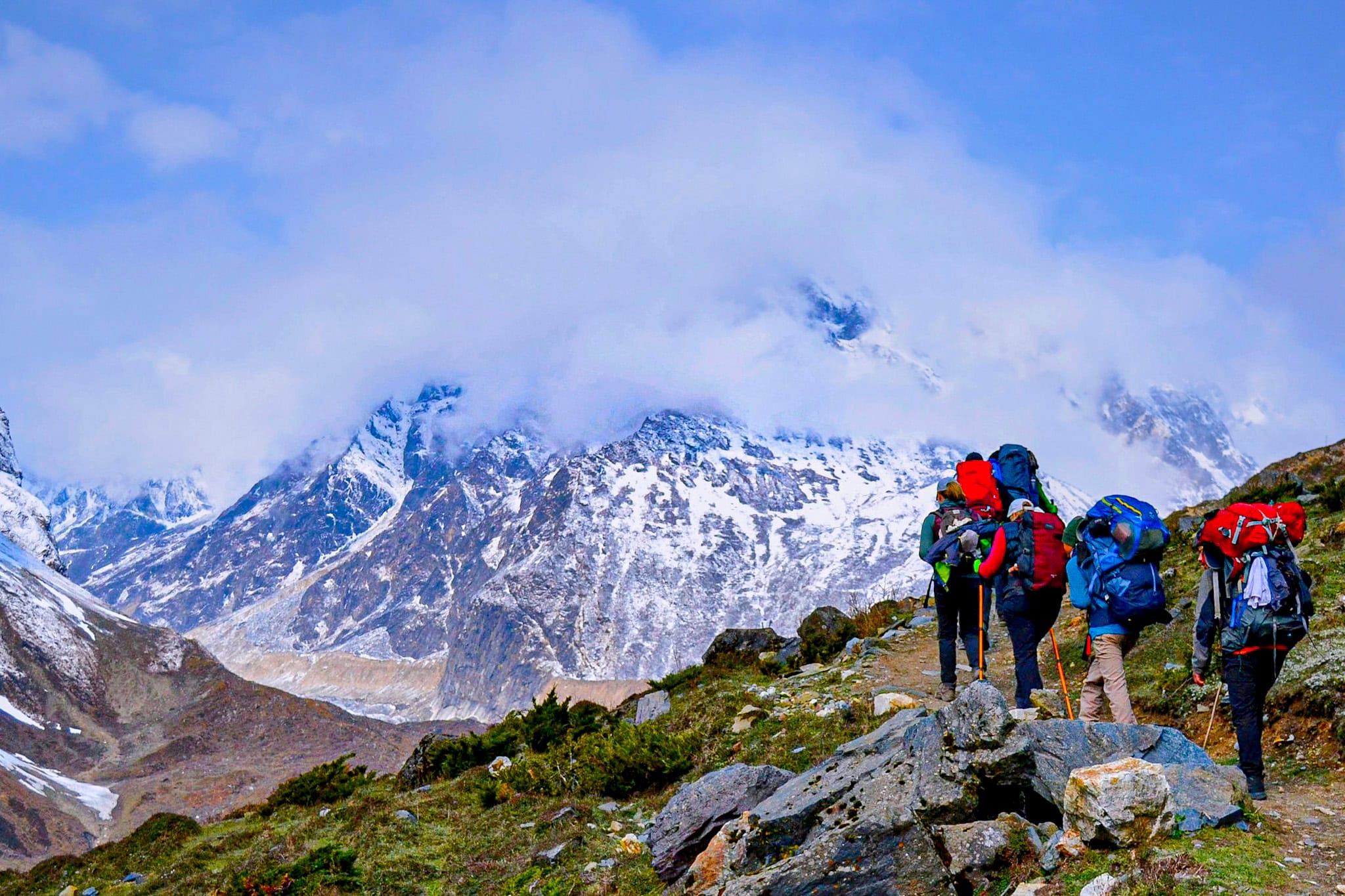 Hikers trekking through mountainous terrain with snow-capped peaks in the background.
