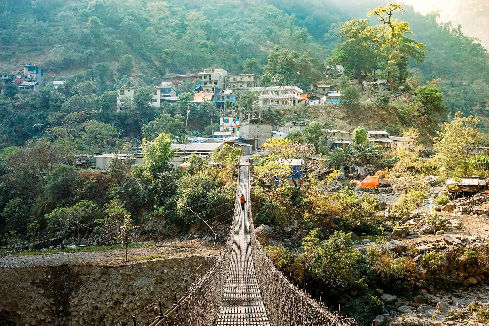 Suspension bridge leading to a hillside village surrounded by lush greenery.