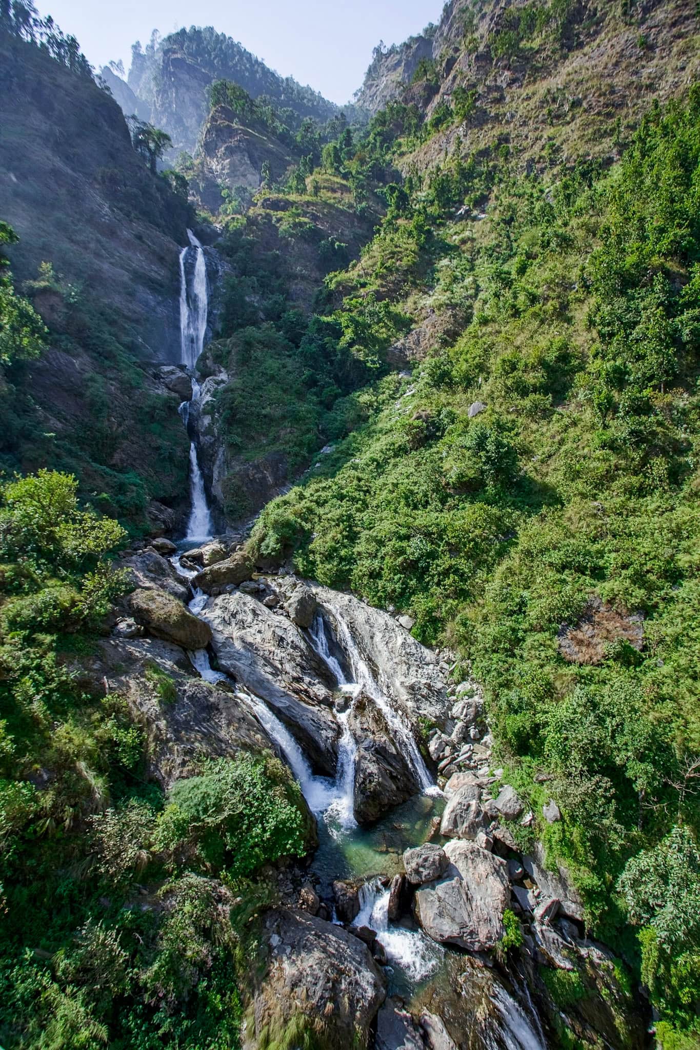 Serene mountain waterfall surrounded by lush green forest in a remote natural setting.