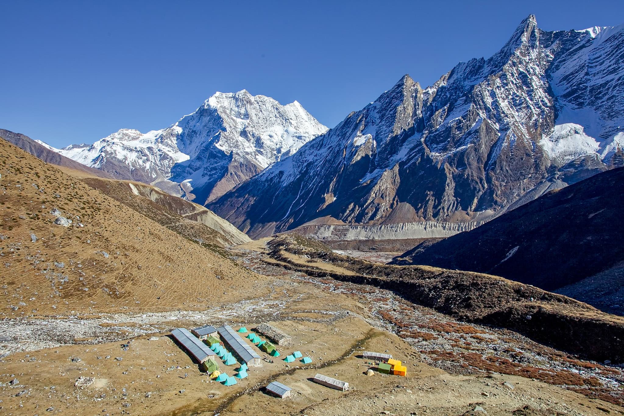 Snow-capped mountains and alpine tents at a high-altitude base camp in the Himalayas.