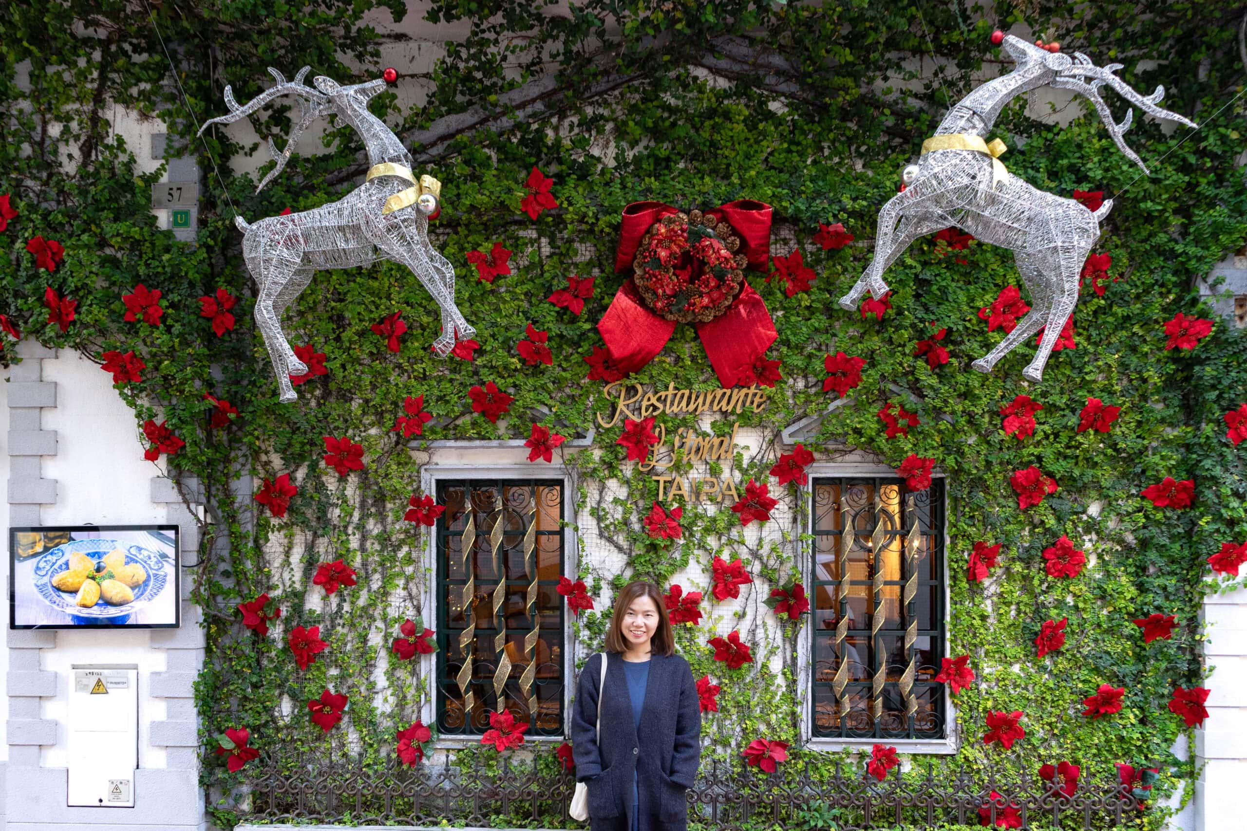 Jin stands in front of Restaurante Litoral in Taipa. There are Christmas decorations between the ivy growing up the wall