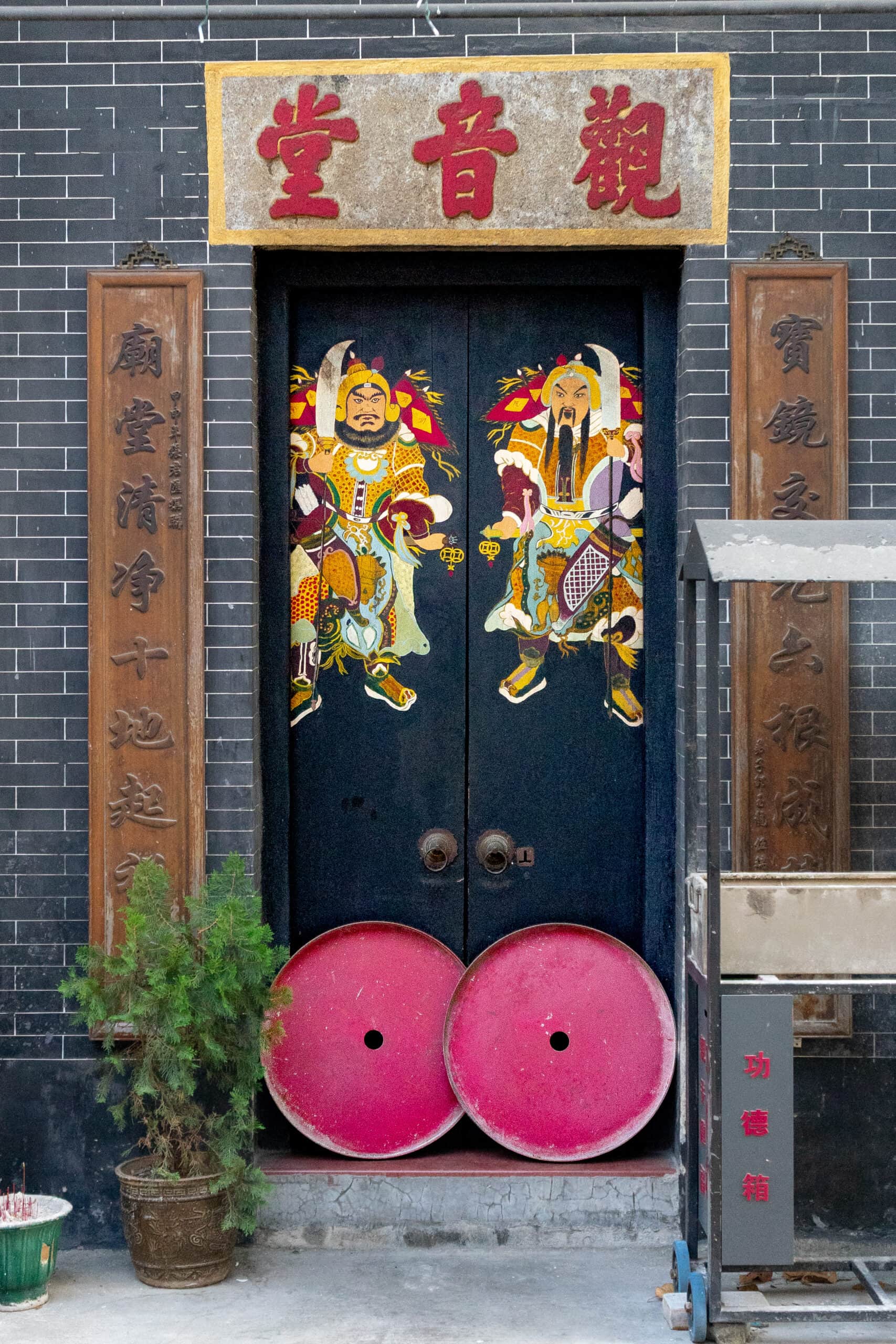 Black temple doors with two colourful guardians painted on them, seen at a temple in Macau