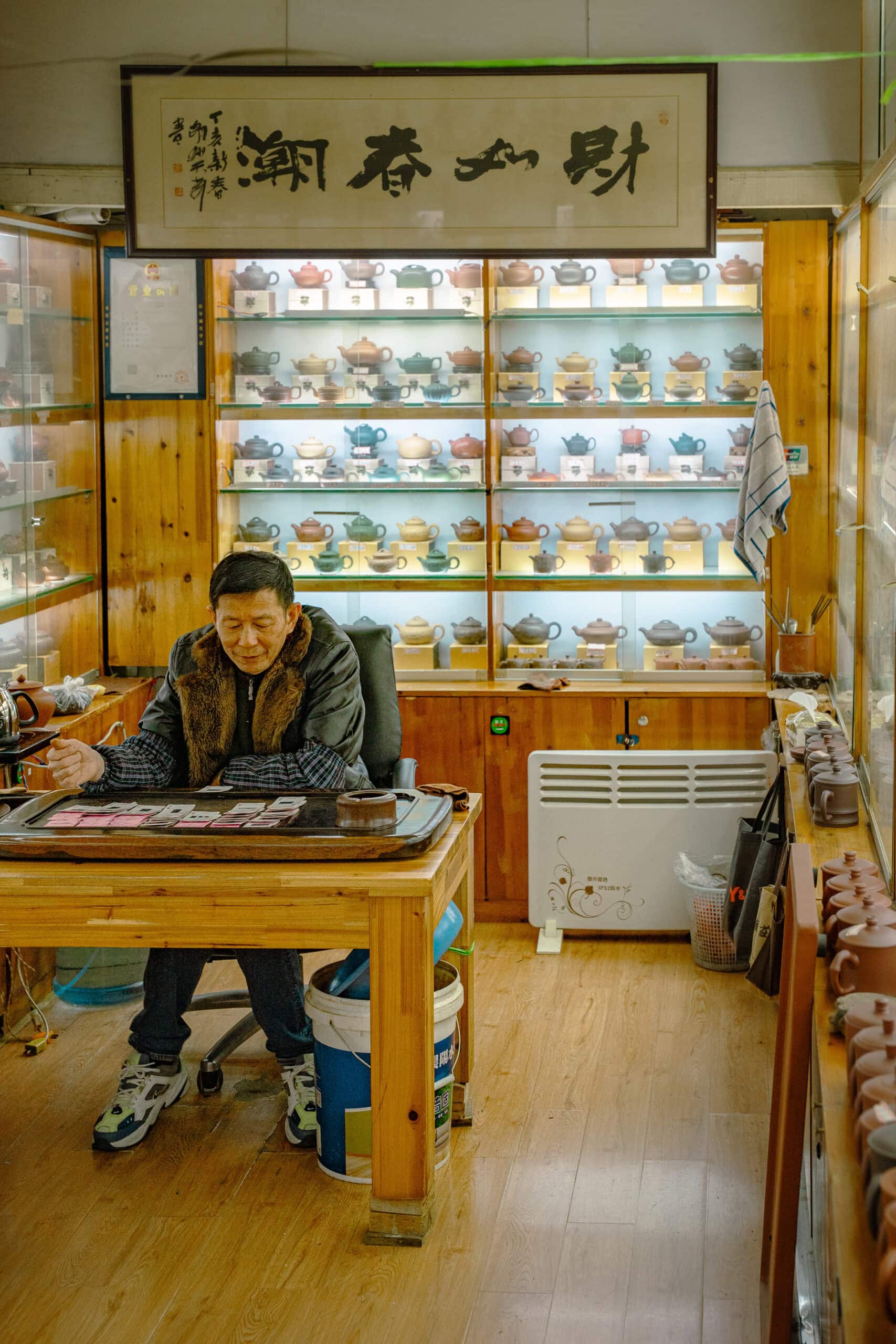 A shop owner plays cards while waiting for customers at The Tianshan Tea City in Shanghai. Behind him is a display cabinet full of small Yixing clay tea pots