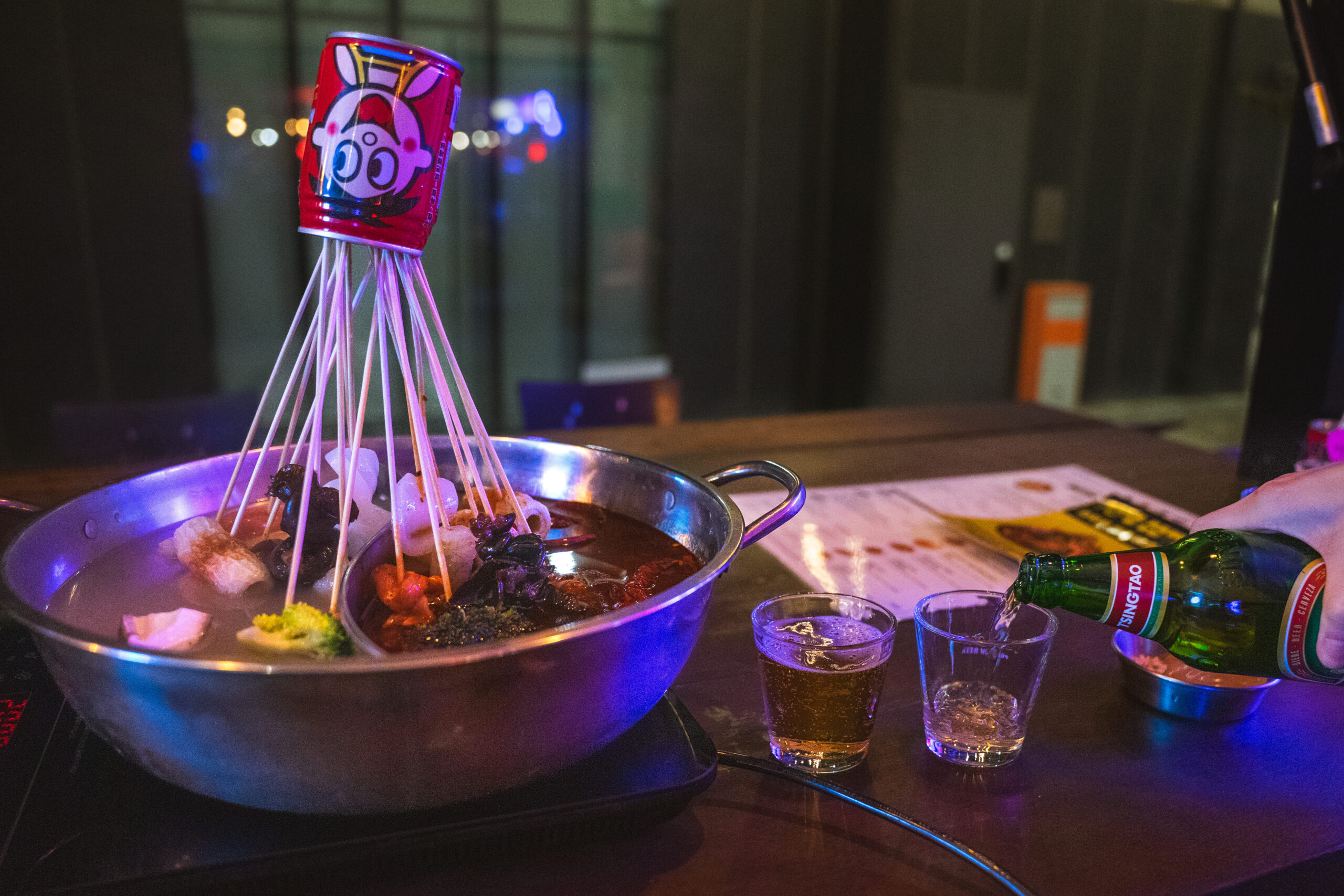 Jin pours Tsingtao beer into two small glasses next. toour boiling skewer hot pot