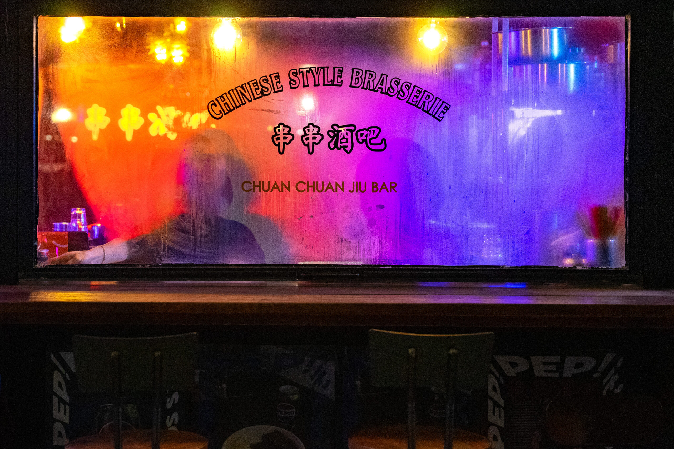 Jin sitting behind a steamed up window and neon lights at Chuan Chuan Jiu Bar in Euljiro. The photo looks very artistic, like something from an Art Movie