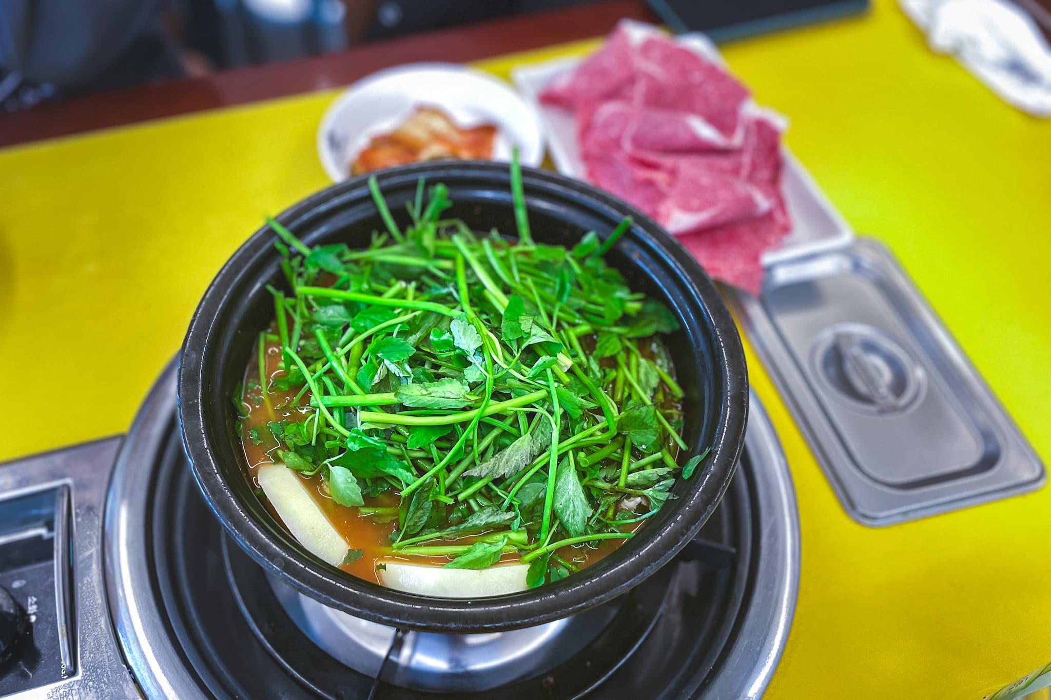 A pot filled with broth and topped with water parsley (minari) sitting on a portable stove