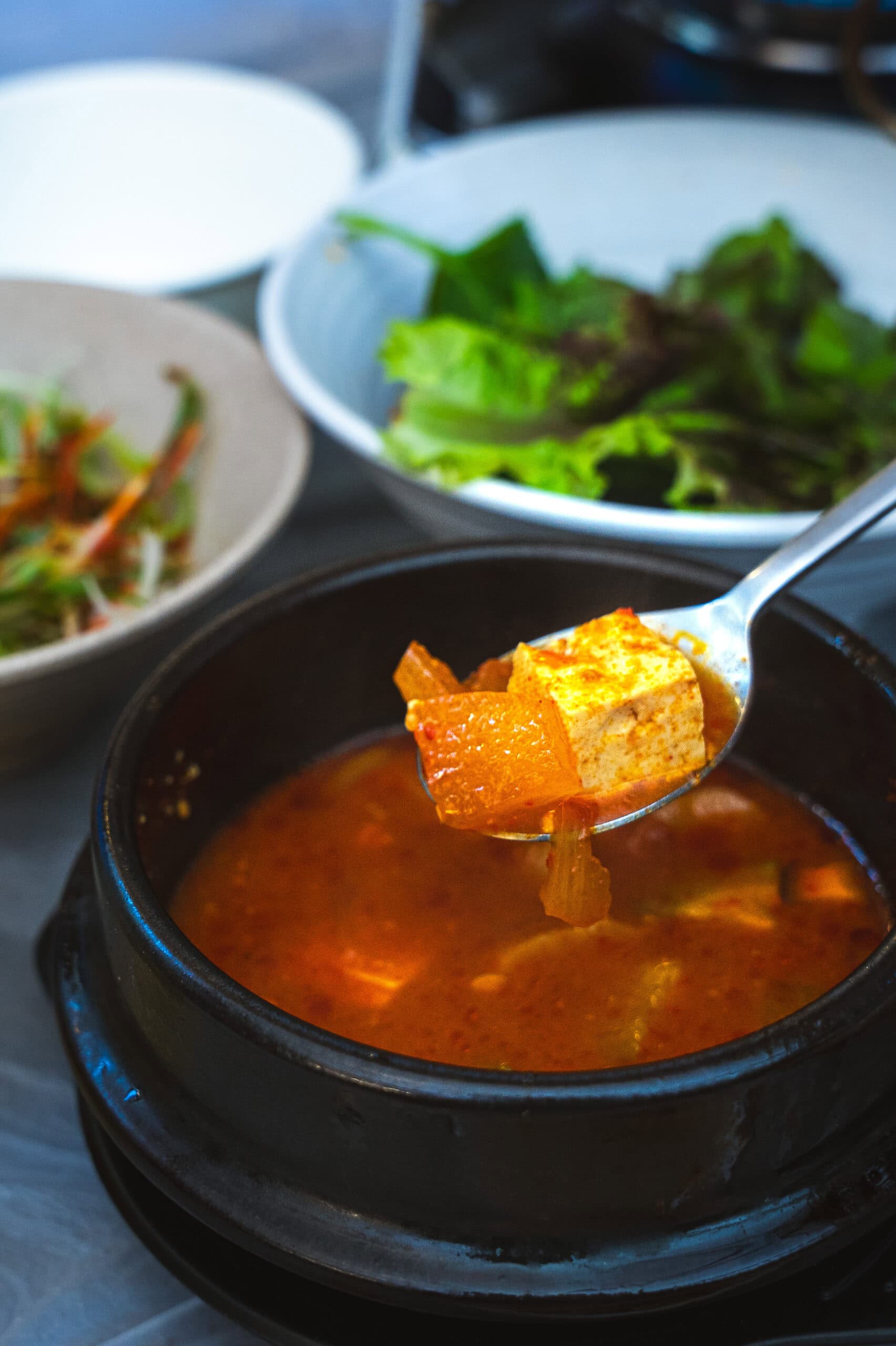 a close up of a cube of tofu sitting on a spoon over a bowl of Doenjang-jjigae (