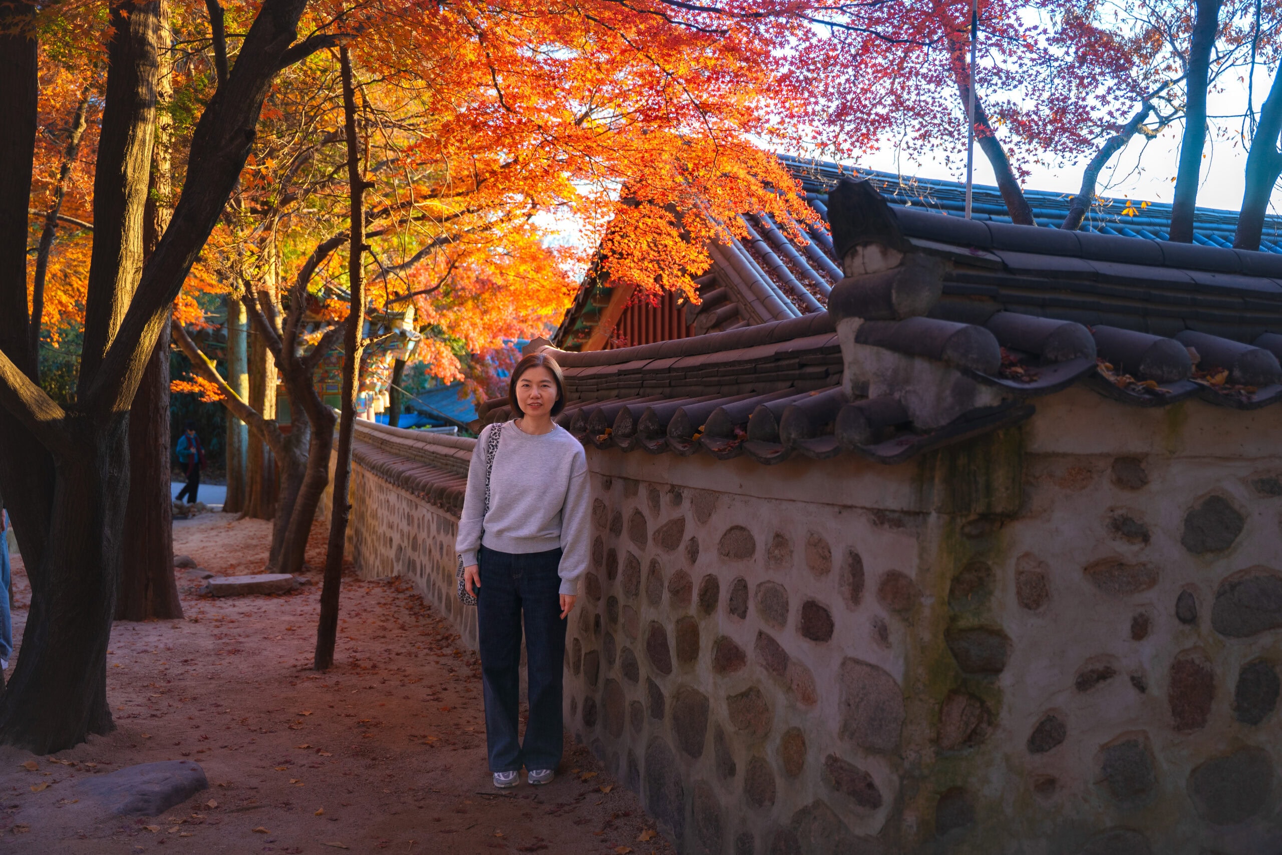 Jin standing under orange maple leaves next to a temple wall of