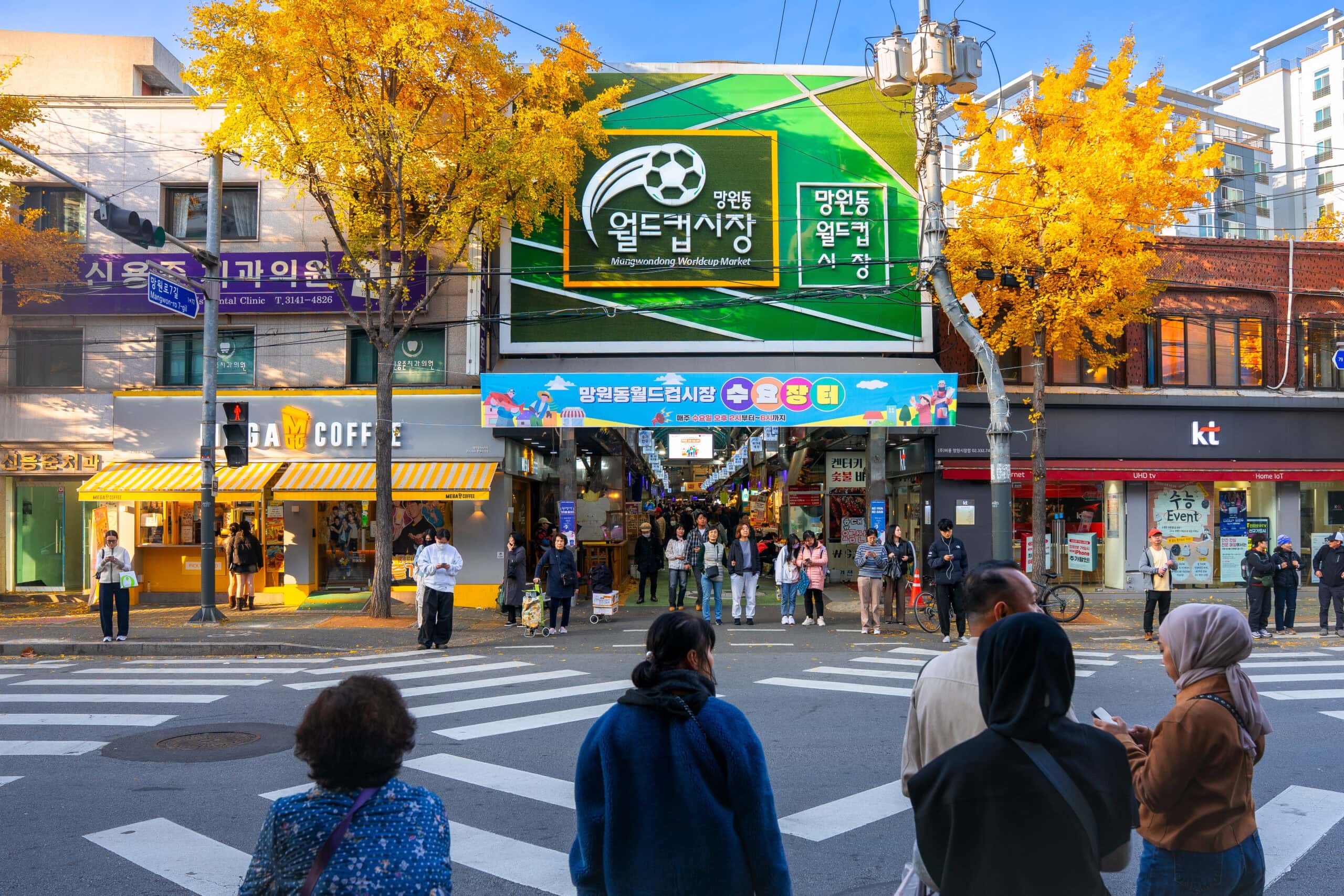 The entrance to the Mangwon world cup stadium market on a clear fall day. You can see two bright yellow ginkgo trees framing the entrance