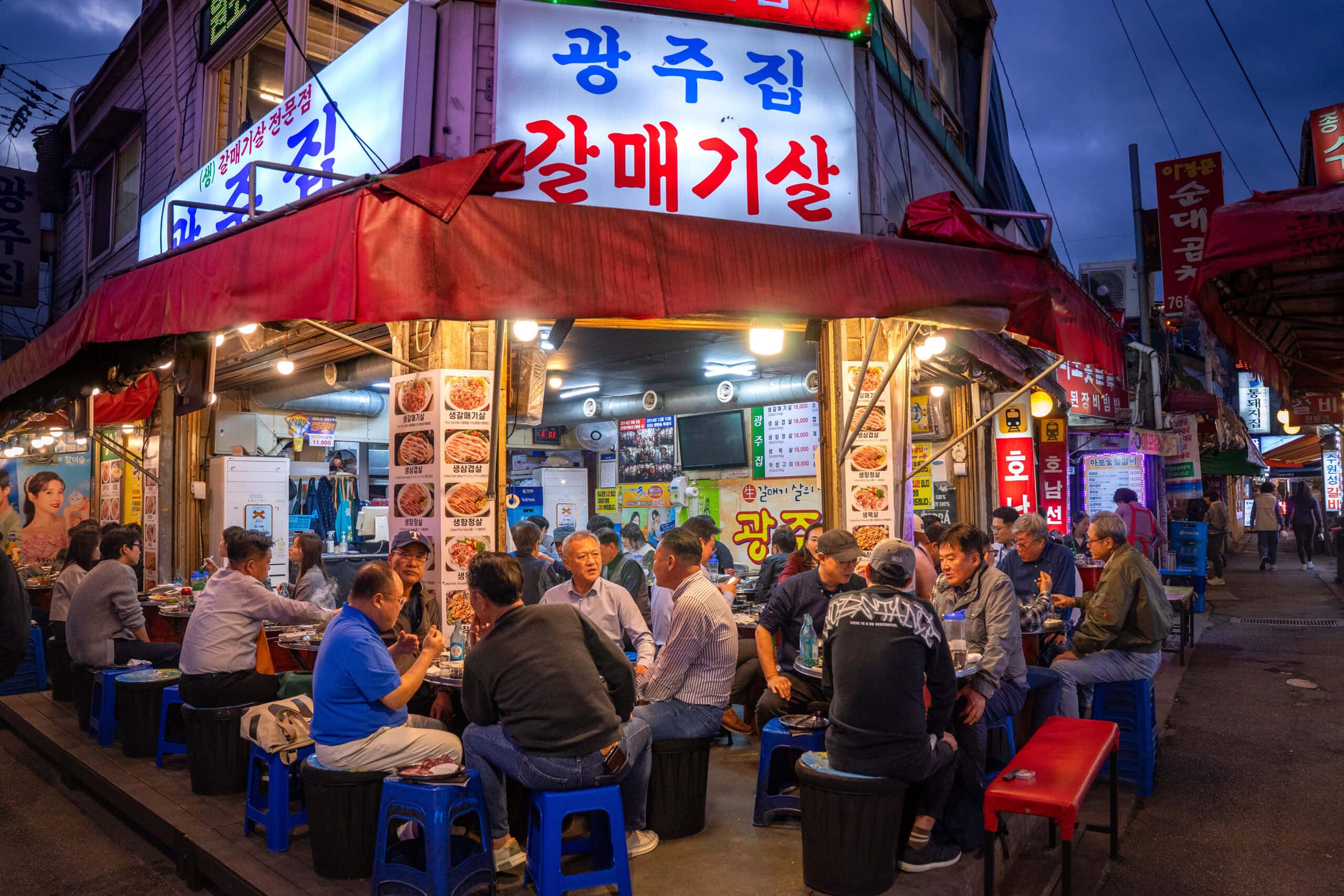 People sit on plastic stools outside a packed korean BBQ restaurant in central Seoul in the early evening