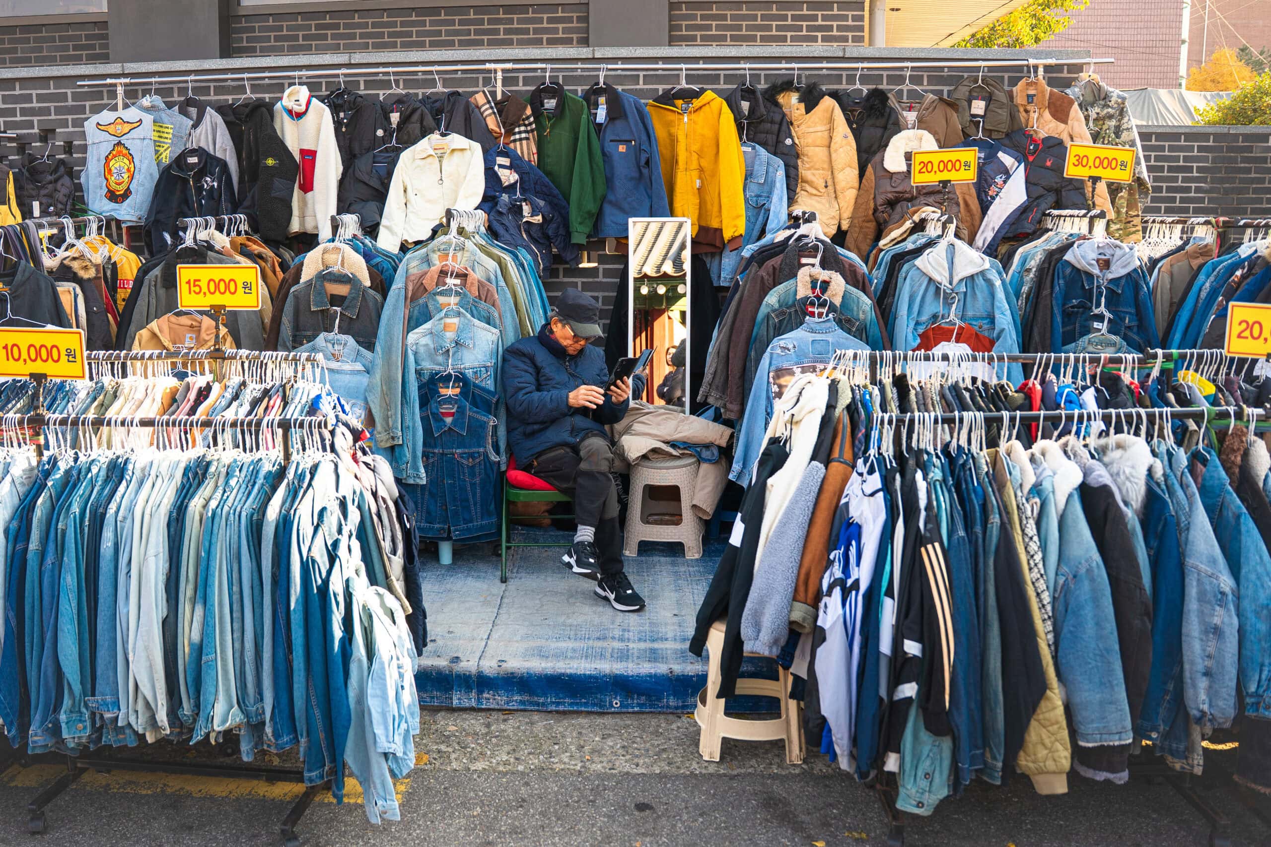 A vendor selling vintage denim in Dongmyo market scrolls his phone while waiting for customers