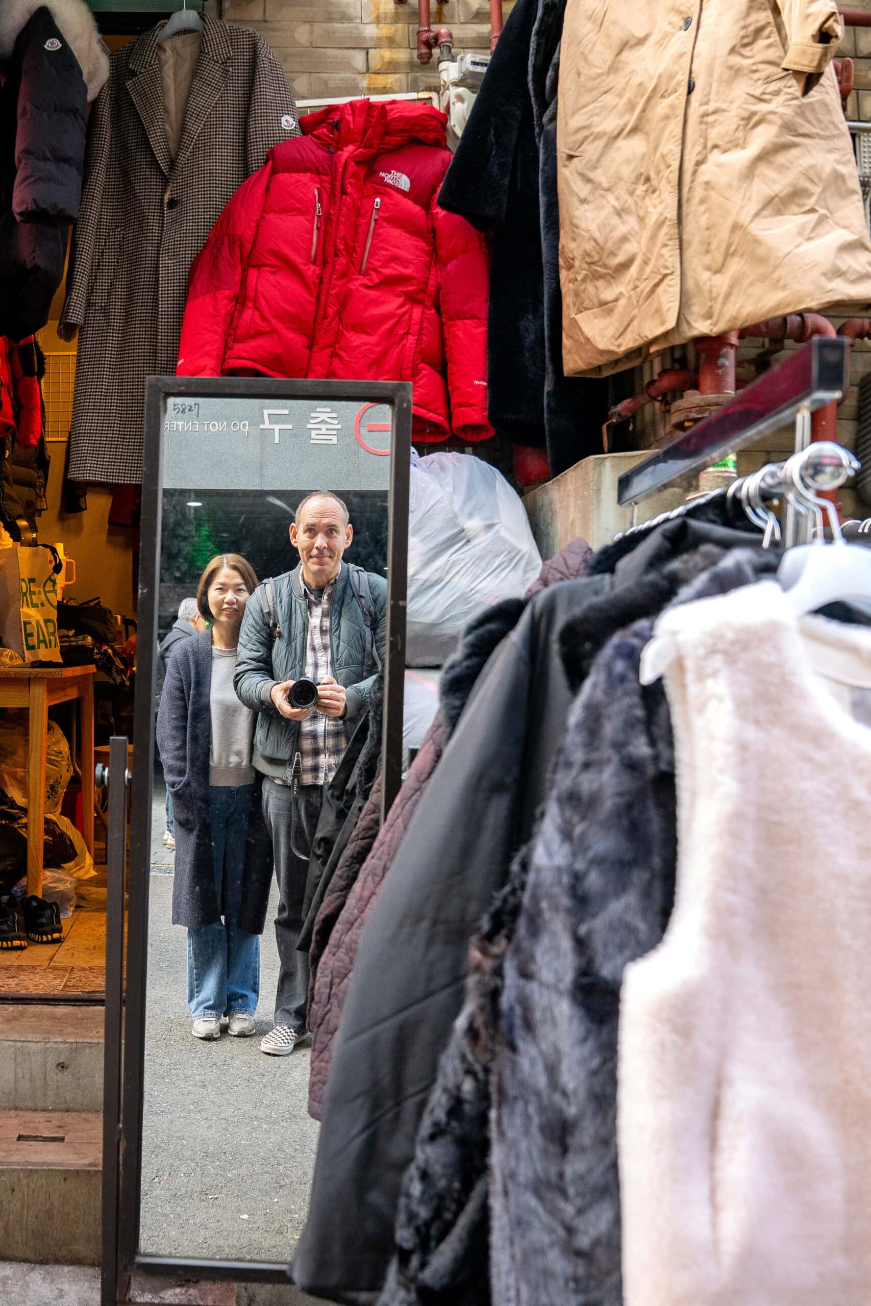 I am taking a photo of Jin and I reflecting in a mirror on the street between second hand clothes, Dongmyo market