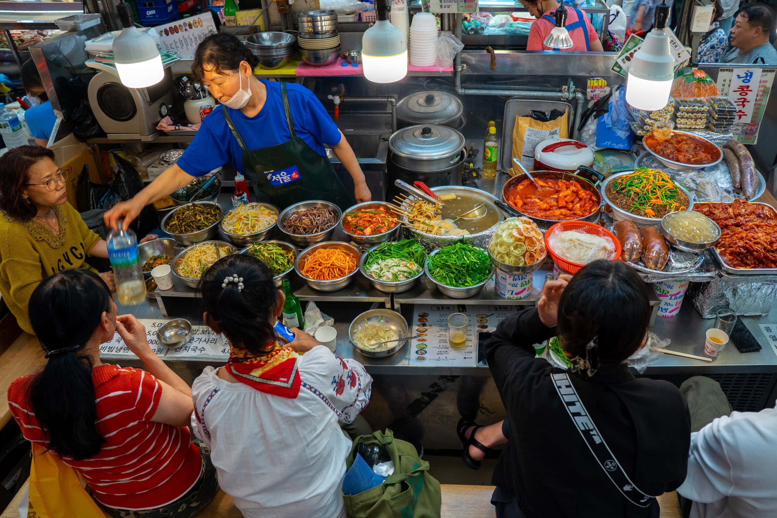 four women sitting at a table filled with traditional Korean food at gwangjang market in Seoul