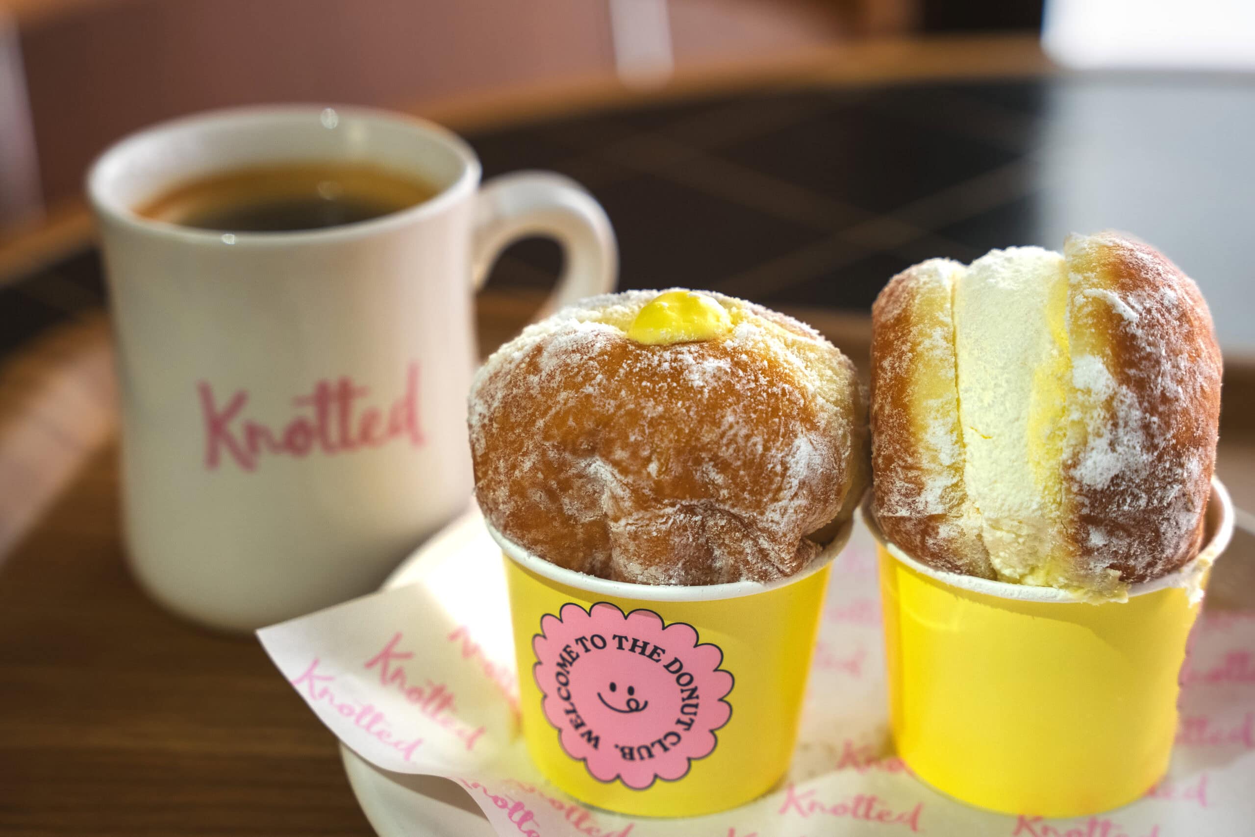 two beautiful, fluffy looking donuts from Knotted sit in ayellow  paper cup each