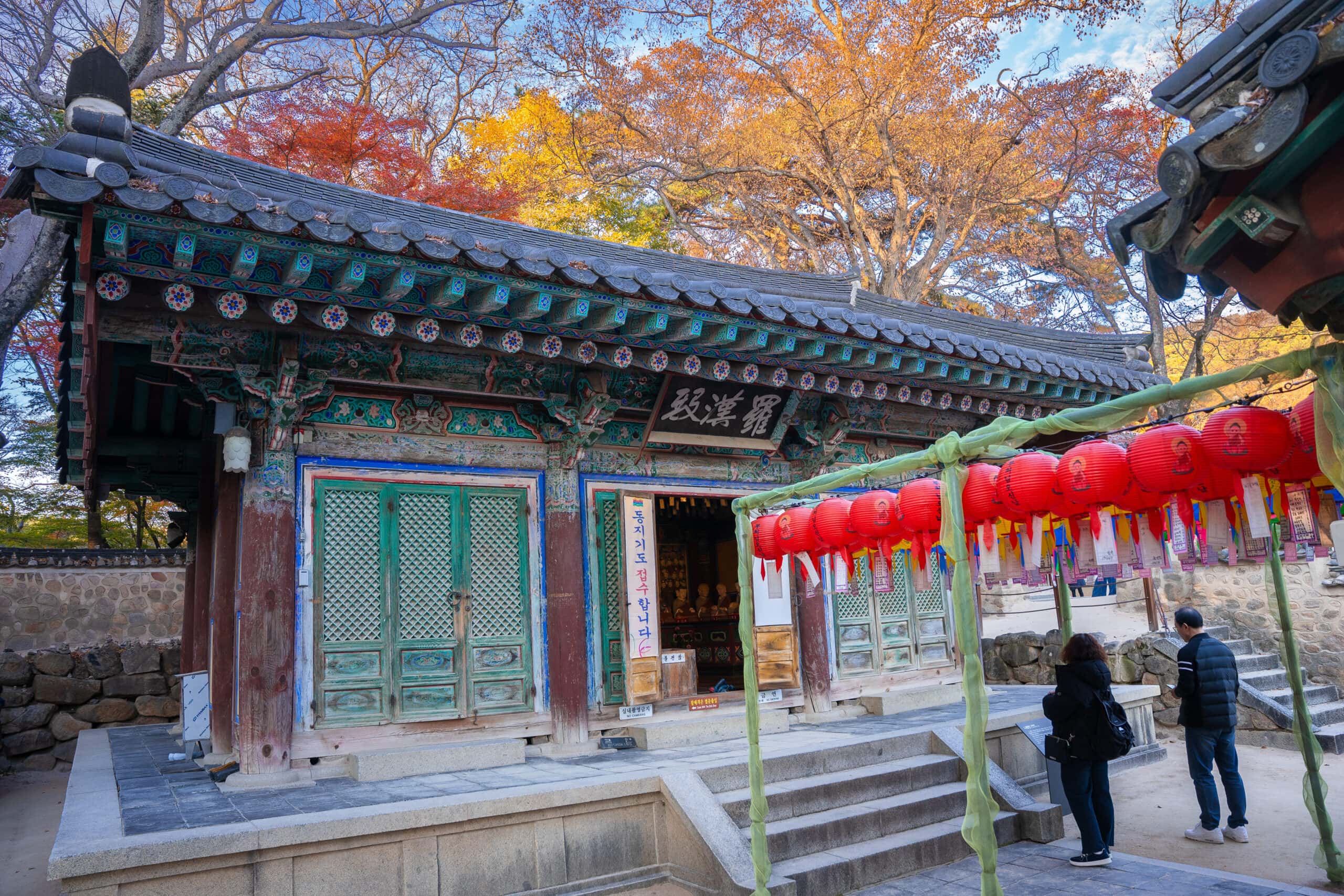 Two people standing beneath red lanterns at a small side temple in Bulguksa