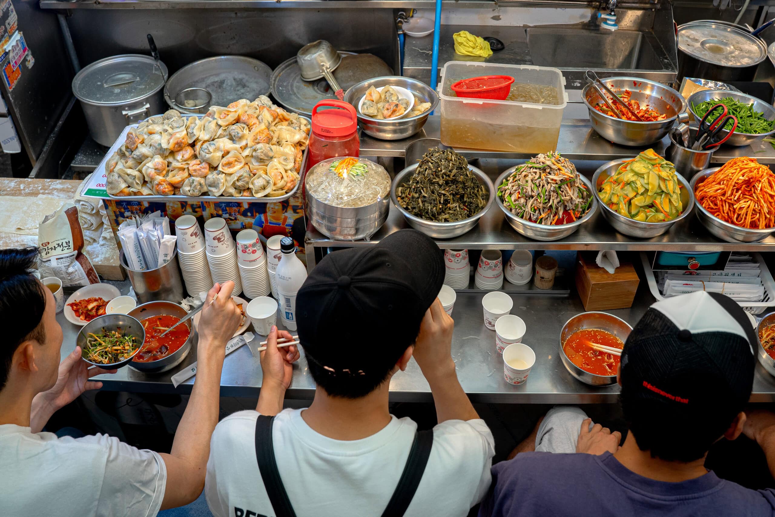 A busy Gwangjang Market stall showcasing what to eat in Seoul, including fresh mandu dumplings and traditional Korean side dishes.