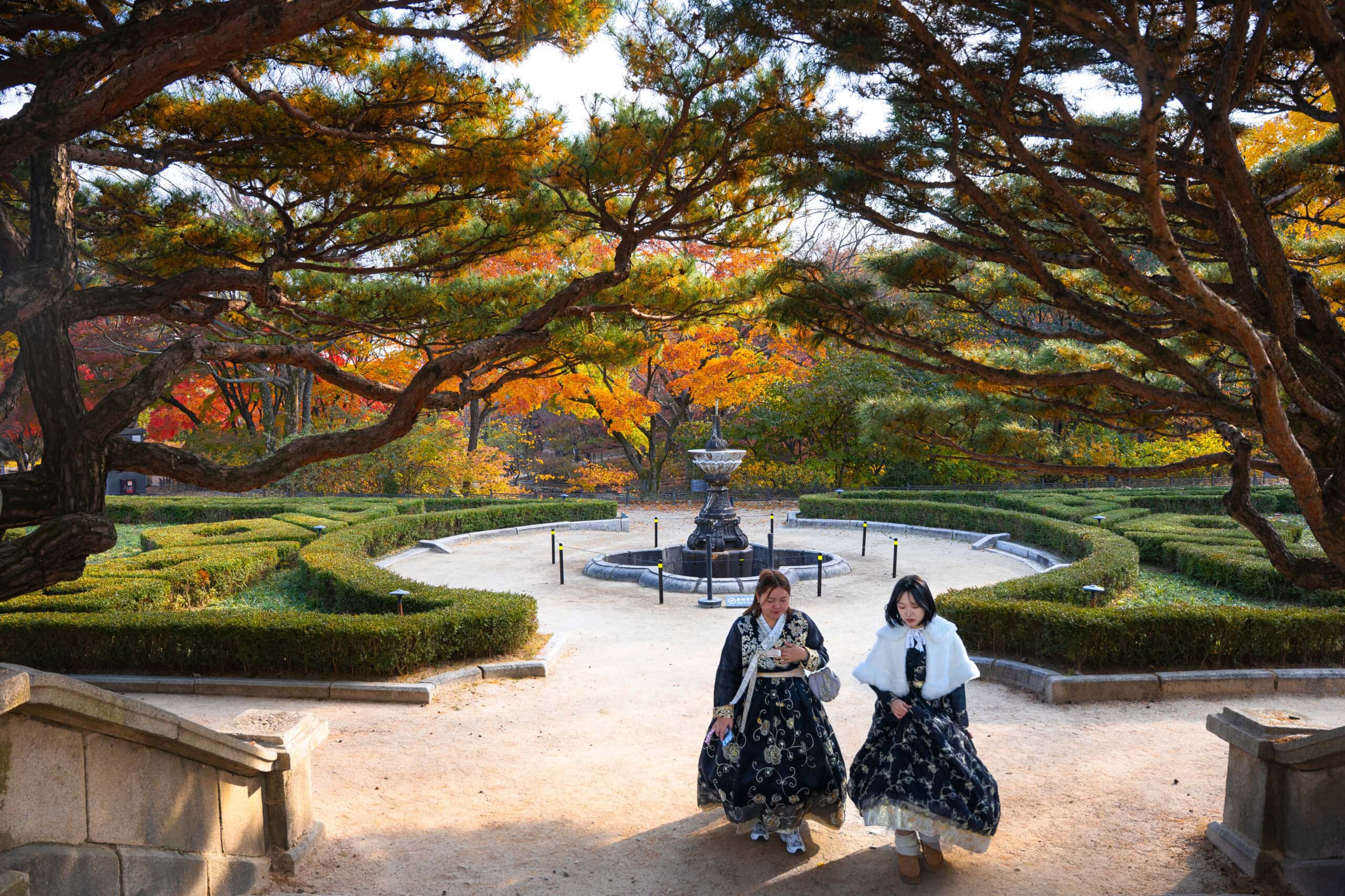 Two women dressed in winter hanbok walk in a garden in Seoul