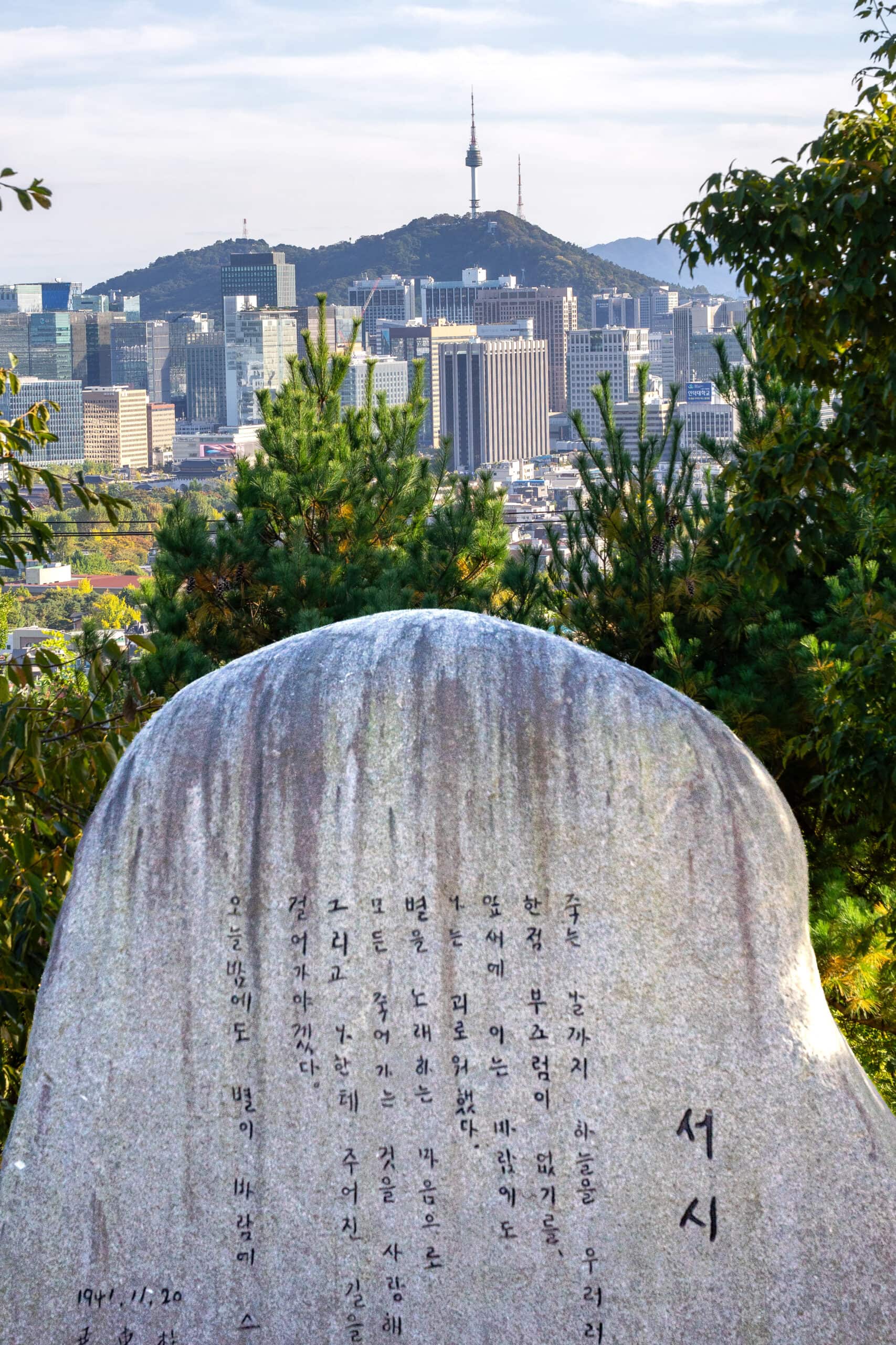 The poem Foreword (Seosi) engraved on a large granite stone stone stands in a park in Buam-dong, with the Seoul skyline and N Seoul tower in background