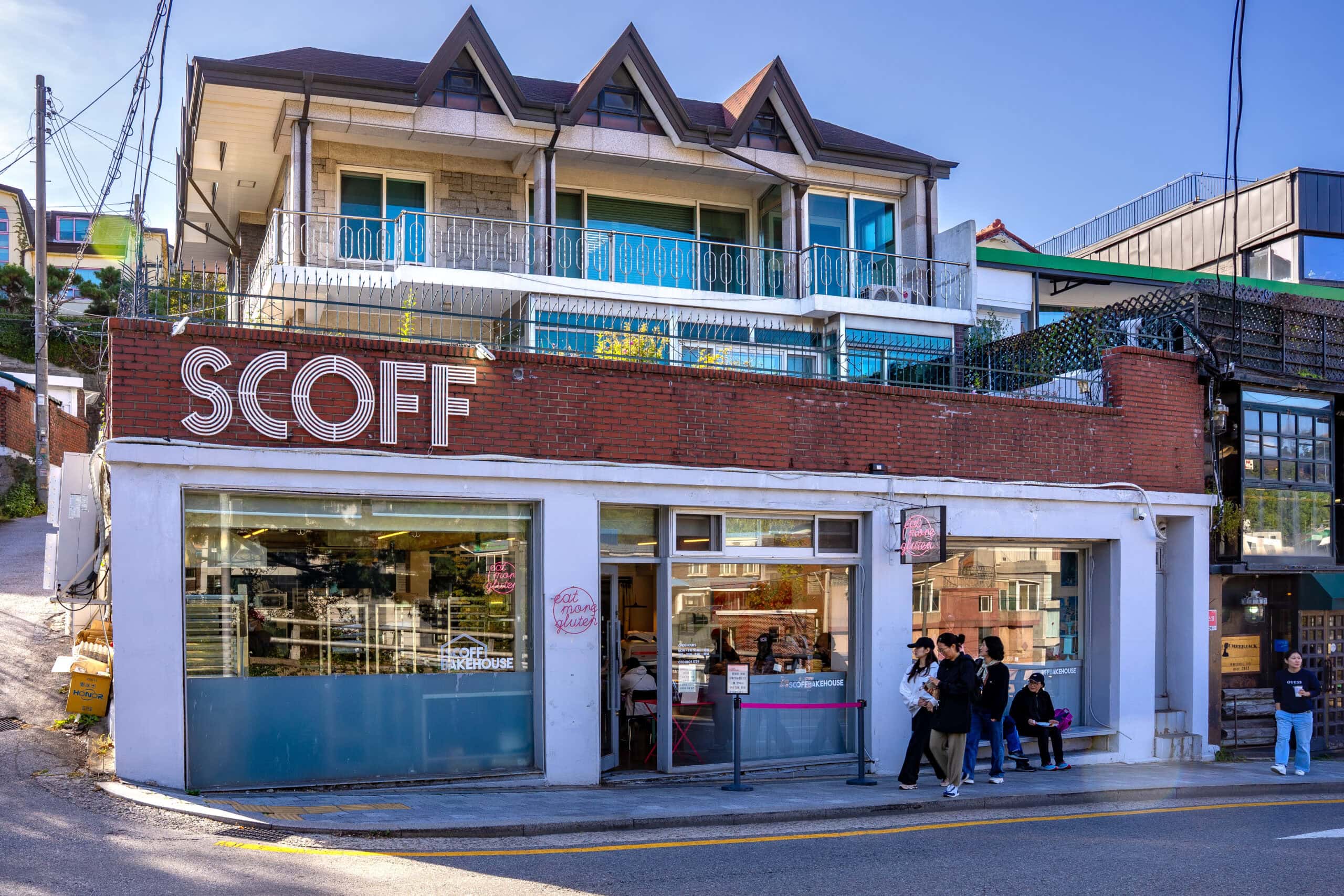 The exterior of Scoff Bakehouse in Buam-dong featuring a red brick facade, large glass windows, and people queueing on the pavement.