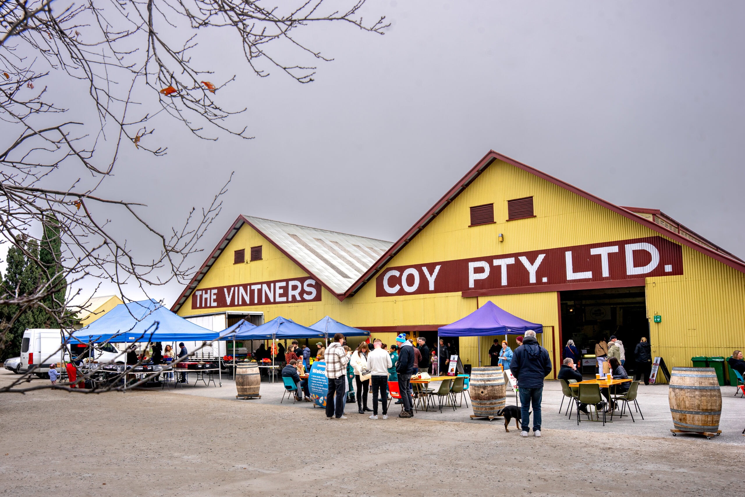 The yellow and brown Vintners shed where the weekly Barossa Farmers Market is held. It's a cold and foggy winter day with people standing outside