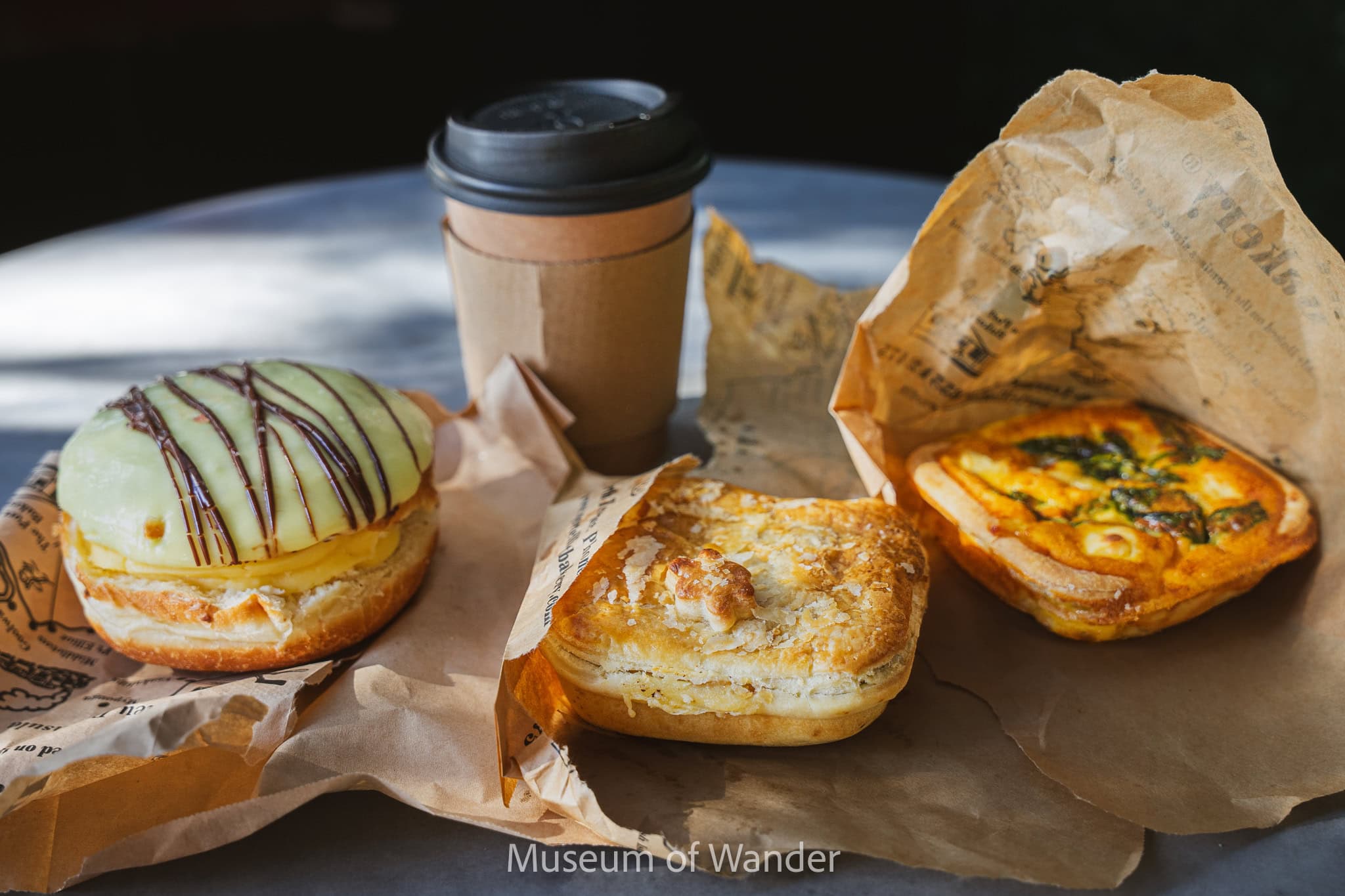 the two pies and one custard Berliner sitting on brown paper bags with a coffee we had at Port Elliot Bakery, South Australia