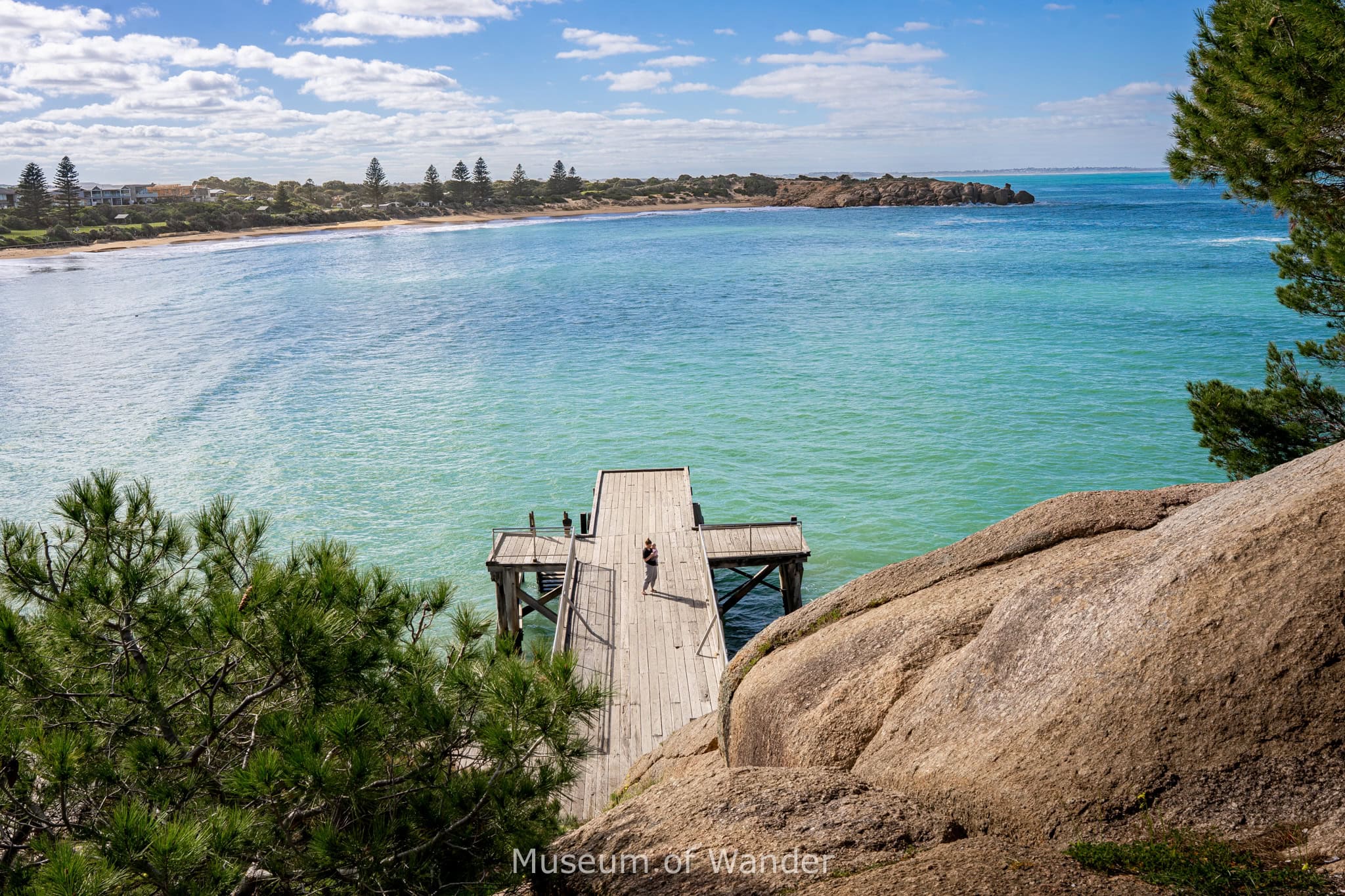 A woman stands on the Horseshoe Bay Jetty in Port Elliot. The water is brilliant blue