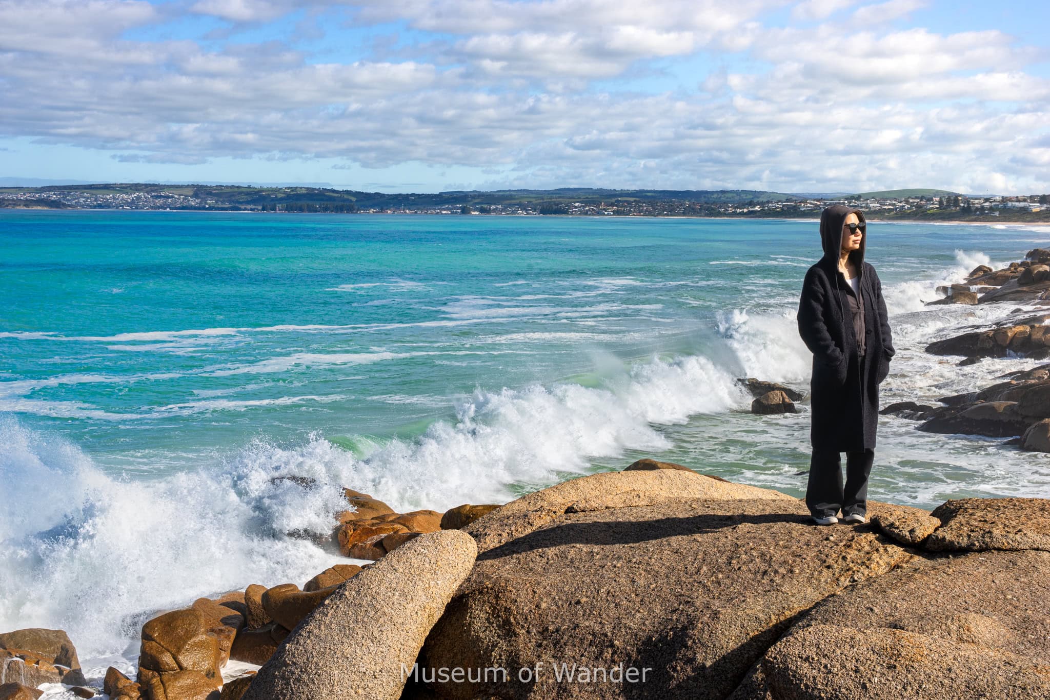 Jin stands on large granite boulders at Freeman's Knob in Port Elliot. You can see large waves smashing into the boulders behind her