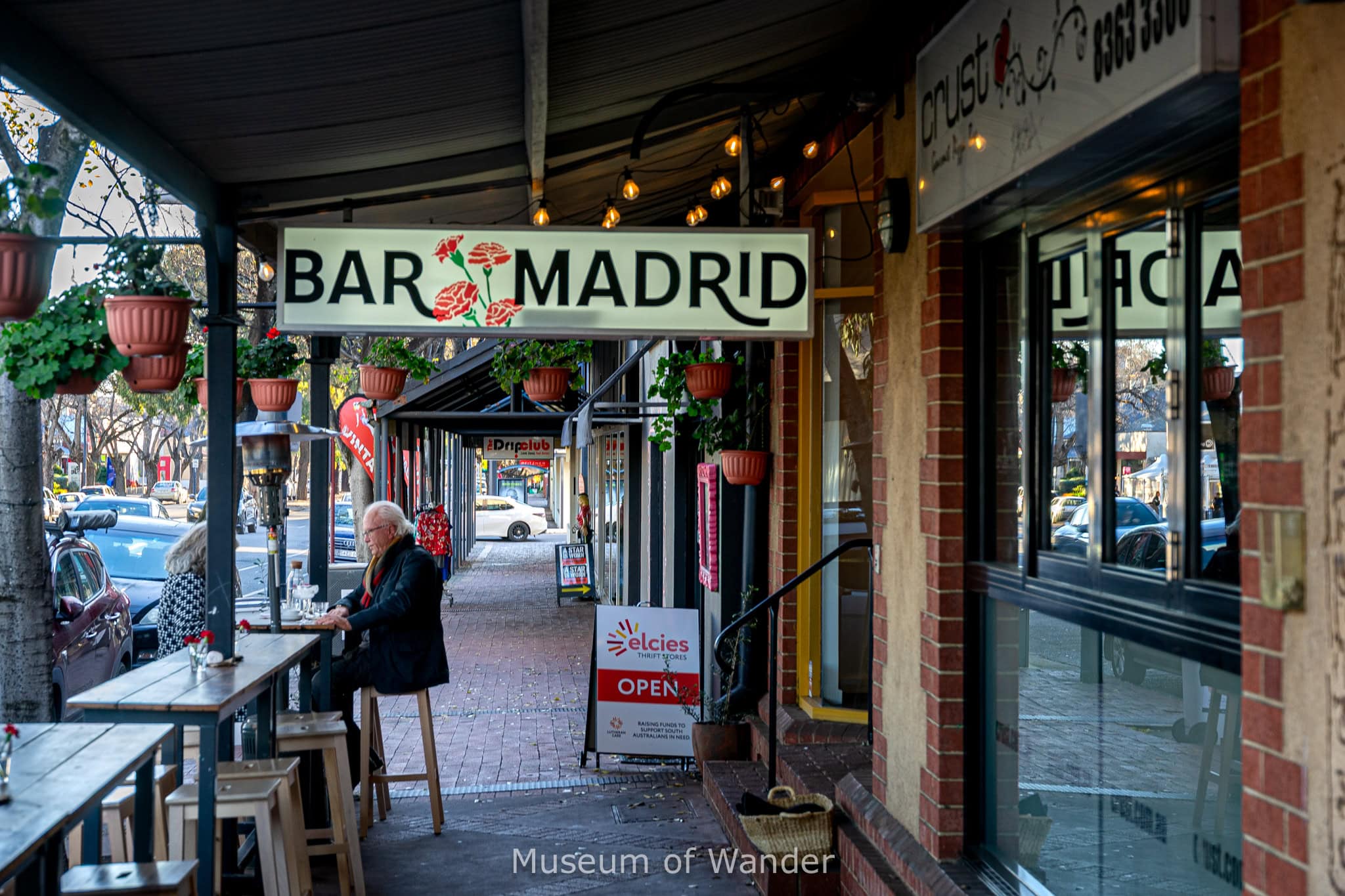An elderly couple sit drinking cocktails under the Bar Madrid sign on the Parade in Norwood, Adelaide, South Australia. This is a great suburb when choosing where to stay in Adelaide