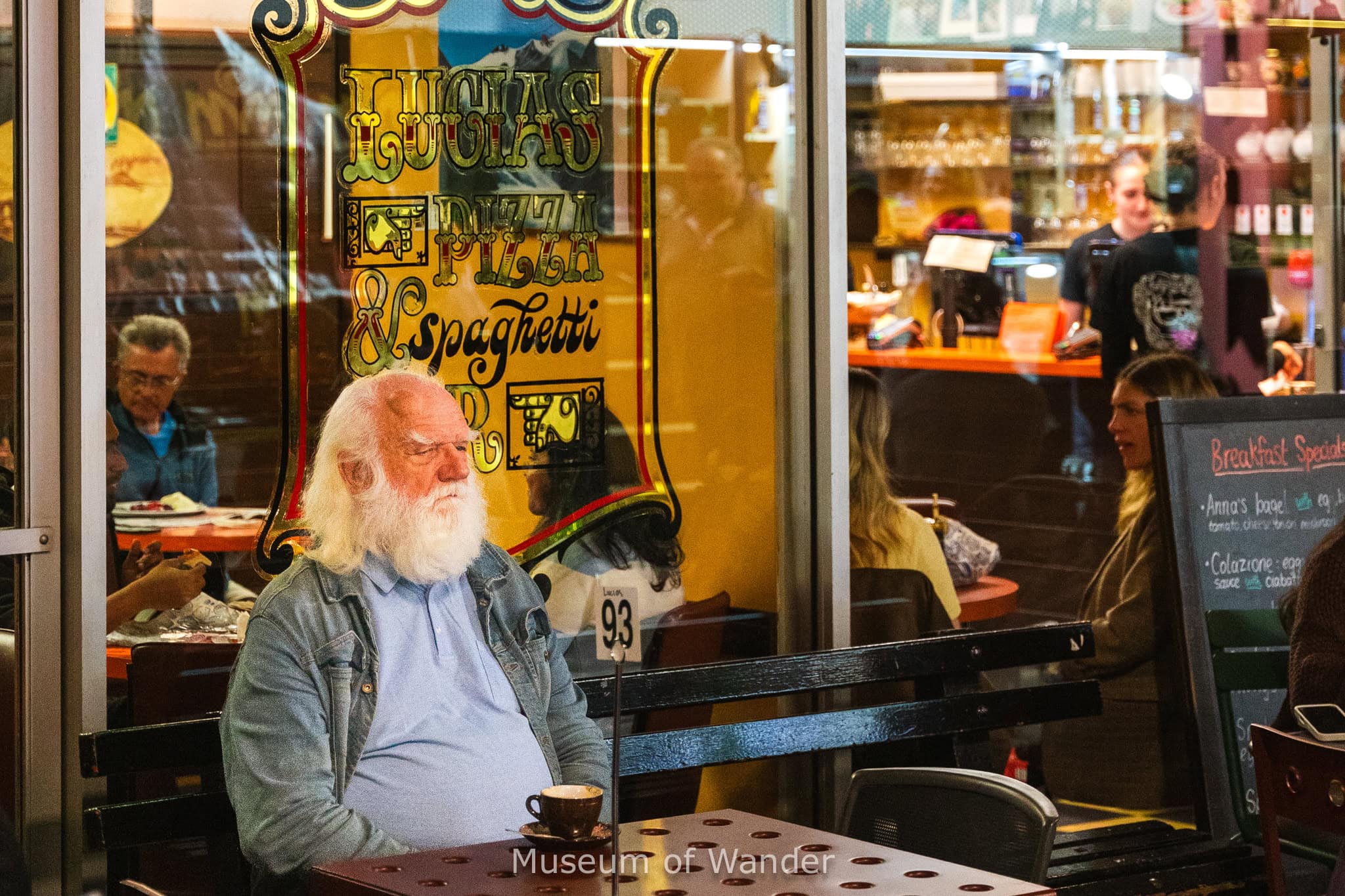 A man with a big white beard sits with his coffee in front of the famous Lucias Pizza and Spaghetti Bar. This is one of the most famous restaurants in Adelaide Central Market