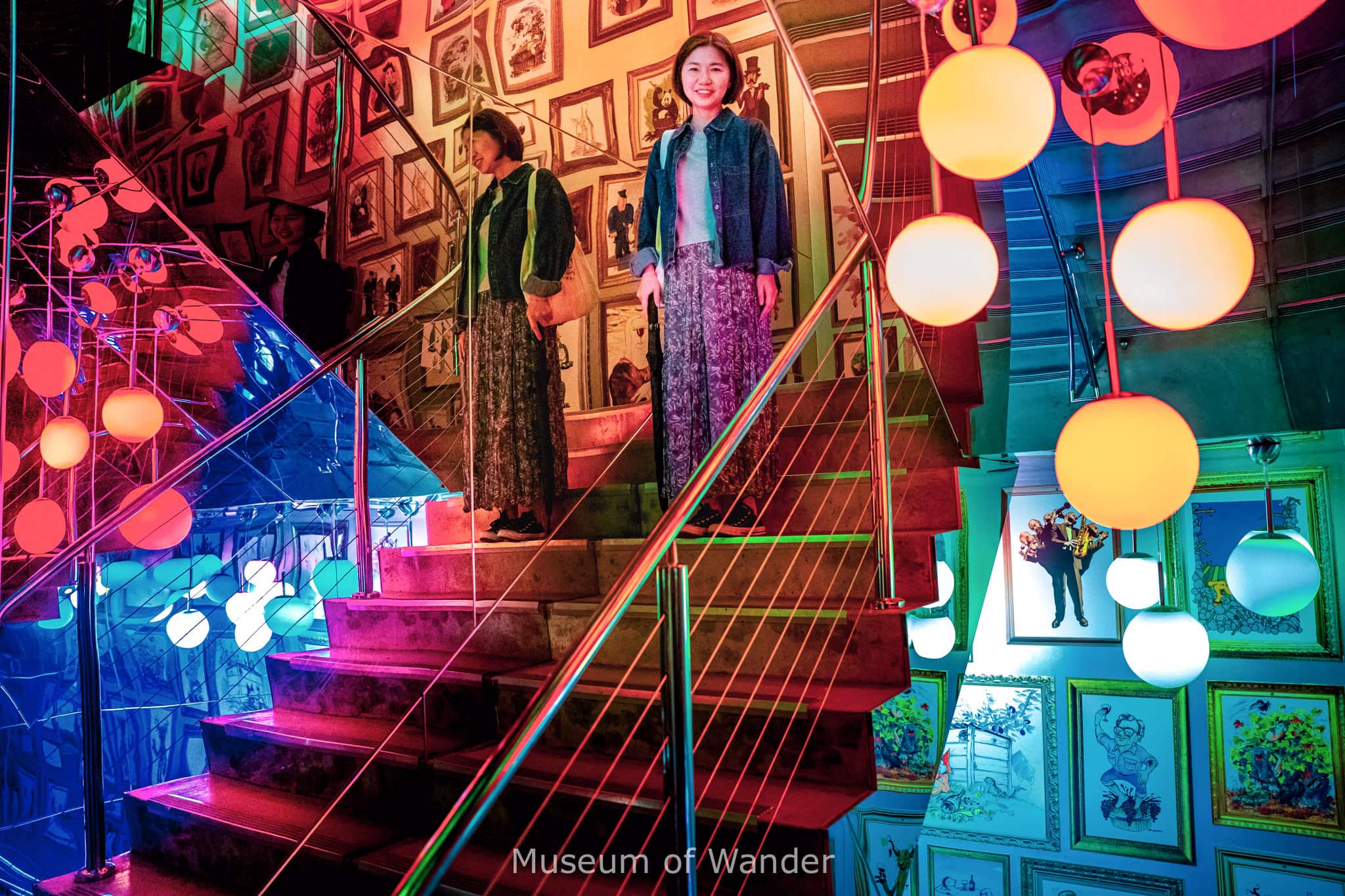 Jin stands on the stairs inside teh d'Arenberg cube. She is surrounded by mirrors, bright red lights and framed pictures