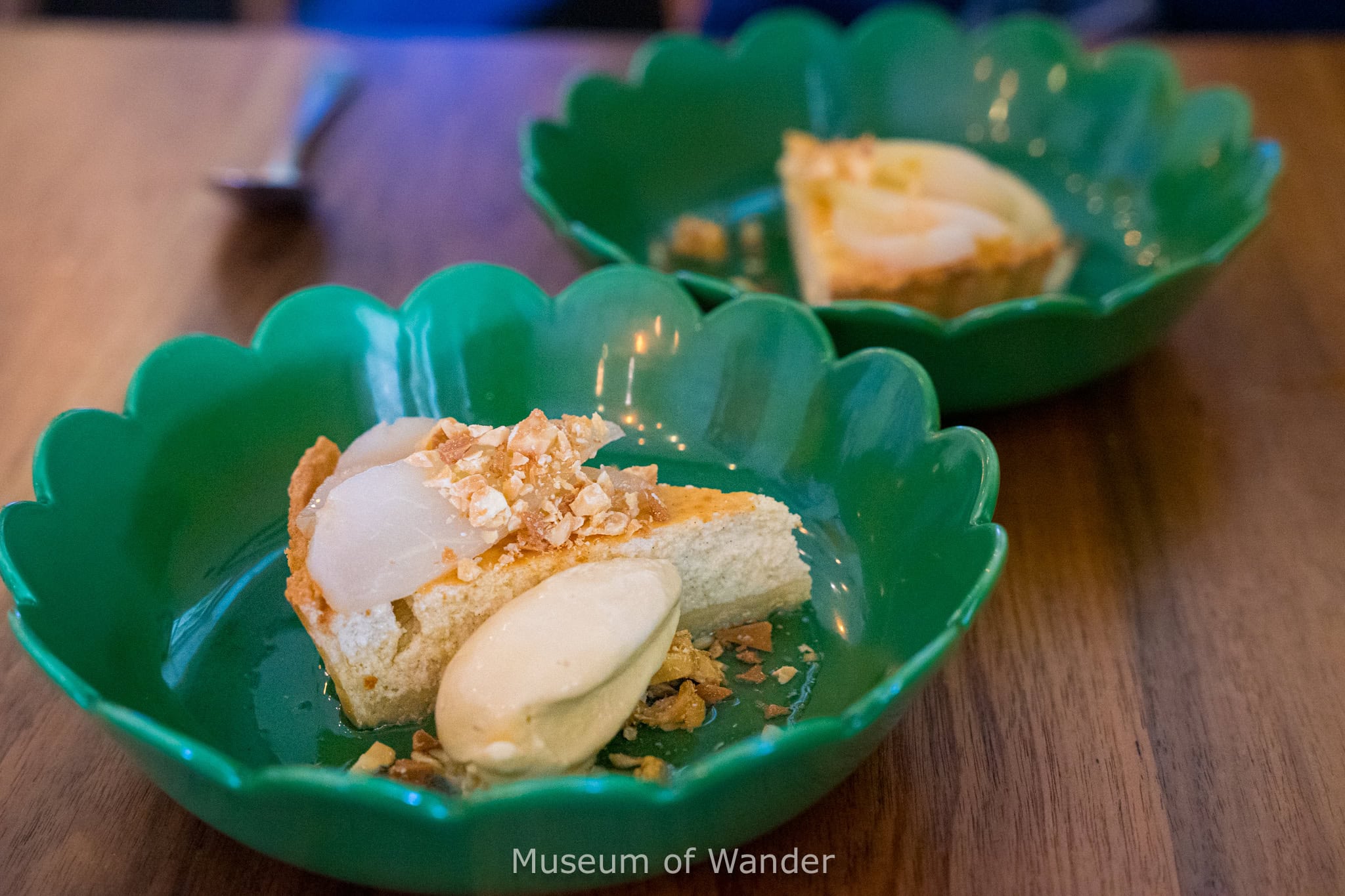 Ricotta cake topped with sliced pears and caramel nuts served with ice cream in a deep green petal shaped plate sitting on a wooden table at Salopian Inn, Adelaide